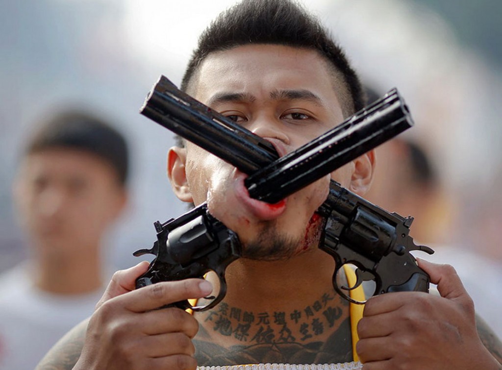 A devotee of the Chinese Bang Neow Shrine with two guns pierced through his cheeks takes a part in procession during the annual vegetarian festival in Phuket