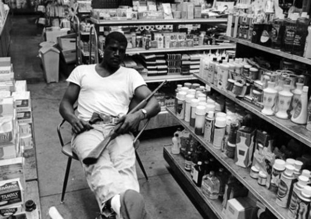 With his .22 hunting rifle on his lap and a revolver in his belt, heavyweight boxer Amos Lincoln, aka Big Train, guards the family drug store during rioting in the Watts area of Los Angeles, August 1965. (Photo by Express/Archive Photos/Getty Images)