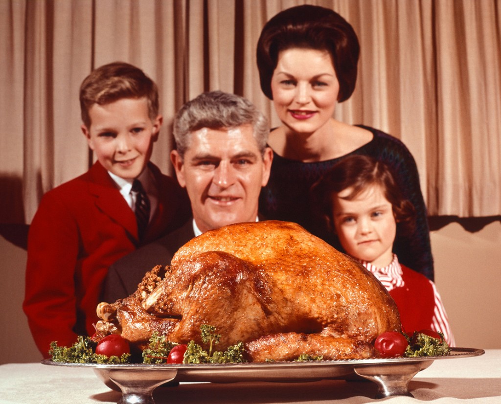 BR9YJ6 1960s PORTRAIT OF FAMILY FATHER MOTHER SON DAUGHTER LOOKING AT THANKSGIVING OR CHRISTMAS ROAST TURKEY